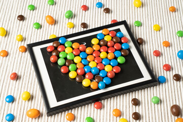 A playful and fun design with small dragee candies arranged like a picture in a frame on a white table.