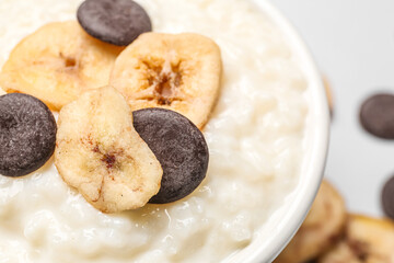Bowl with delicious rice pudding, banana slices and chocolate chips on white background, closeup