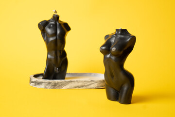 Female and male body shaped candles on yellow background. Black torso candles. Candle of body shape.