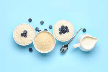 Bowls with delicious rice pudding, blueberries, pitcher and spoon on blue background