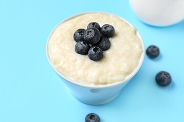 Bowl with delicious rice pudding and blueberries on blue background