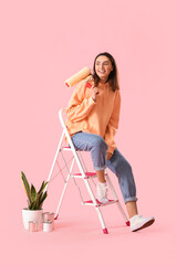 Young woman with paint roller, ladder, cans and houseplant on pink background