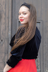Fototapeta premium Mujer joven, blanca, caucásica mirando de frente sonriendo, con labios rojos y cabello castaño muy largo en el exterior.