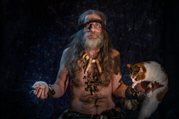 A bearded man with long gray hair holds a rat in his hands and looks at it