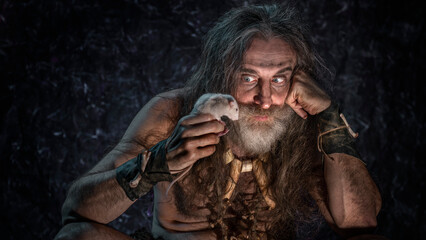 A bearded man with long gray hair holds a rat in his hands and looks at it