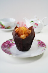 Muffin with tea set on white background. Copy space. Close-up. Selective focus. Yellow citrus muffin on white plate with a floral pattern, space for text.