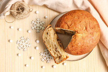 Plate with cut Panettone and Christmas decor on light wooden table, top view