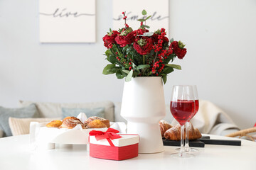 Vase with flowers, pastries, glasses of wine and gift for Valentine's Day on dining table in room