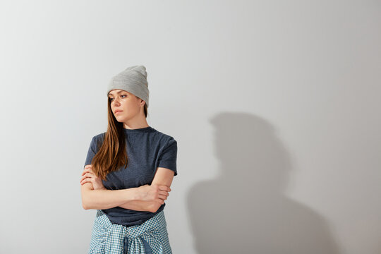 Serious woman in casual tennager clothes and beanie standing with crossed arms and looking at side.