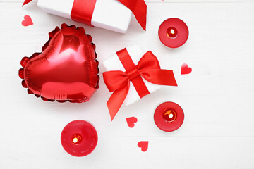 Composition with burning candles, gift boxes and balloon on light wooden background. Valentine's Day celebration