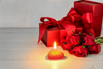 Burning candle, beautiful rose flowers and gift boxes on light wooden table. Valentine's Day celebration