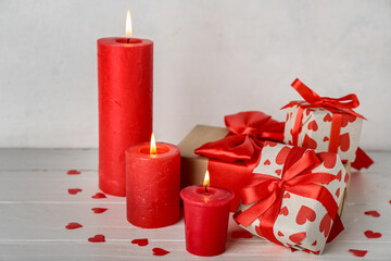 Burning candles, gifts and confetti on light wooden table. Valentine's Day celebration