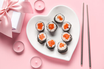Plate with sushi rolls, chopsticks, gift and candles on pink background. Valentine's Day celebration