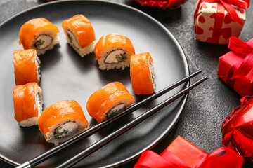 Plate with sushi rolls, chopsticks and gifts on dark background, closeup. Valentine's Day celebration