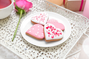 Fototapeta na wymiar Tray with plate of tasty heart shaped cookies and rose flower on table, closeup. Valentine's Day celebration