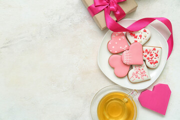 Composition with plate of tasty heart shaped cookies, gift box and cup of tea on light background. Valentine's Day celebration