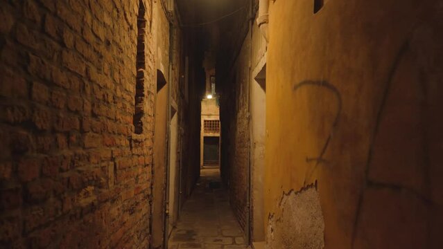 Long dark narrow Venetian street passage between ancient brick and ruined buildings with single lamp illuminating way Venice Italy