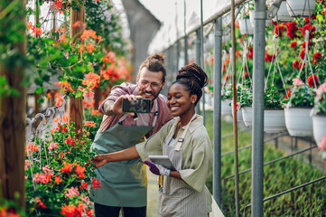 Multiracial florists working in a green house plant nursery and using smartphone