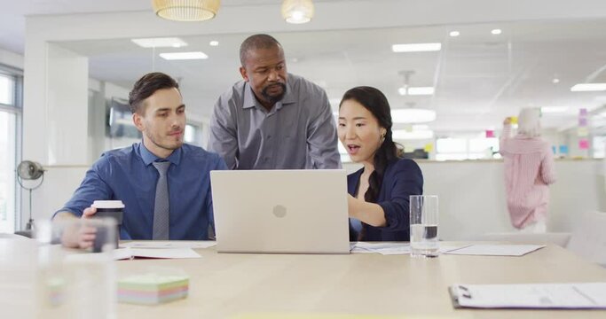 Group of diverse business people using laptop and talking in office, slow motion