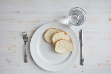 White plate with three slices of bread and a glass of water on a white wood table with copy space...