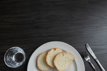 White plate with three slices of bread and a glass of water on a dark wood table