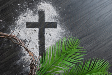 Cross of ashes with partial crown of thorns and palm fronds on a dark wood background with copy...