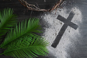 Christian cross of ashes and a partial crown of thorns with green palm leaves on a dark wood...