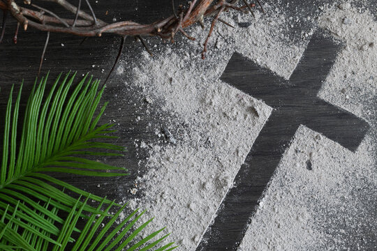 Lent background with cross of ashes, palm leaves and partial crown of thorns on dark wood