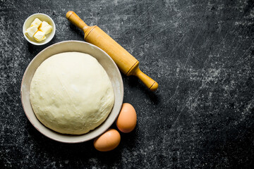 Dough in bowl with eggs, rolling pin and butter.