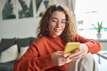 Young smiling woman wearing glasses holding smartphone using cellphone modern technology, looking...