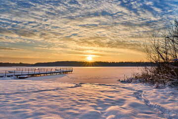 Sunset clouds over frozen lake. Sunset colors reflection in snow covered lake. Frozen lake pier on sunset