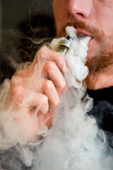 Close up of man smoking a vape device breathing out vape cloud