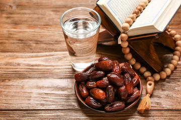 Plate with dates, glass of water, prayer beads and Koran for Ramadan on wooden background, closeup