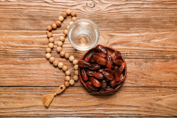 Plate with dates, glass of water and prayer beads for Ramadan on wooden background