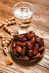 Plate with dates, glass of water and prayer beads for Ramadan on wooden background, closeup