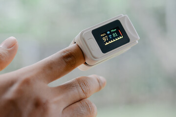 A man's index finger clamped with oximeter shows the oxygen level more than 95% oxymeter