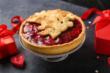 Stand with sweet strawberry pie, cookie hearts, heart-shaped candle, gifts and red ribbon for Valentine's day on dark background