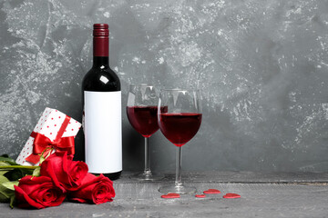 Glasses of wine, bottle, rose flowers and gift box on blue table. Valentine's Day celebration