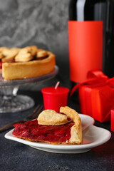 Heart-shaped plate with piece of sweet strawberry pie, cookie hearts, gift and romantic candle for Valentine's day on dark table