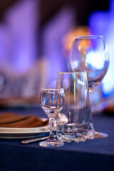 Festive Christmas, wedding, birthday table setting with blue tablecloth, orange napkin cutlery, white plates, glasses for wine, water and strong alcoholic beverages.