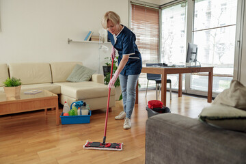 Professional housemaid in uniform washing floor with mop in living room