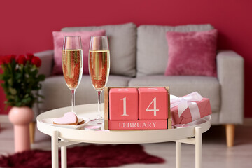 Calendar with date 14 FEBRUARY, glasses of champagne, cookies and gift on table in living room, closeup