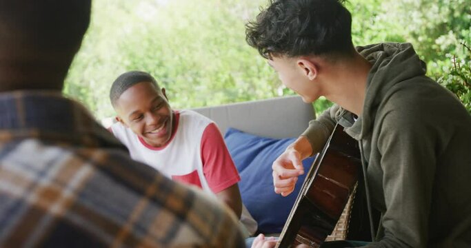 Happy diverse male teenage friends playing guitar at home, slow motion