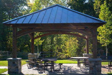 Gazebo or pavilion in a park with some seating and tables providing shade and rest - obrazy, fototapety, plakaty