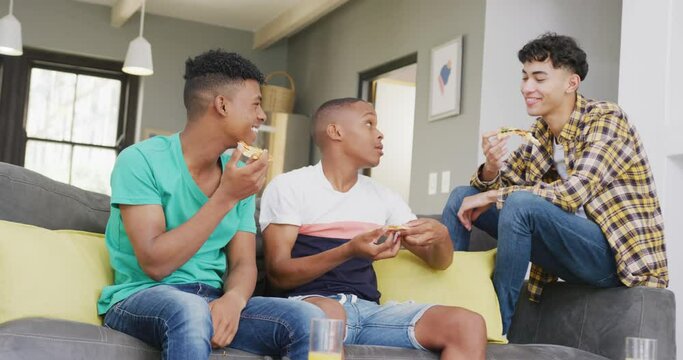 Happy diverse male teenage friends eating pizza and sitting on couch, slow motion