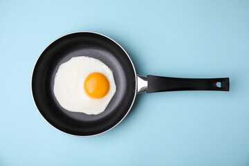 Tasty fried egg in pan on light blue background, top view