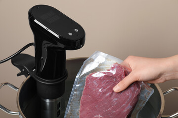 Woman putting vacuum packed meat into pot with thermal immersion circulator, closeup. Sous vide...