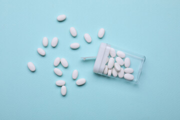 Tasty dragee candies and container on light blue background, flat lay