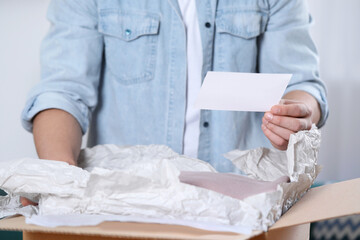 Man holding greeting card near parcel with Christmas gift, closeup