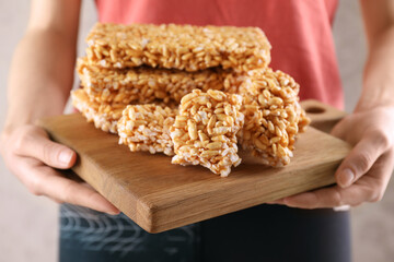 Woman holding wooden board with puffed rice bars (kozinaki), closeup